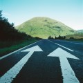 Two painted arrows on a road pointing towards a grassy mountain